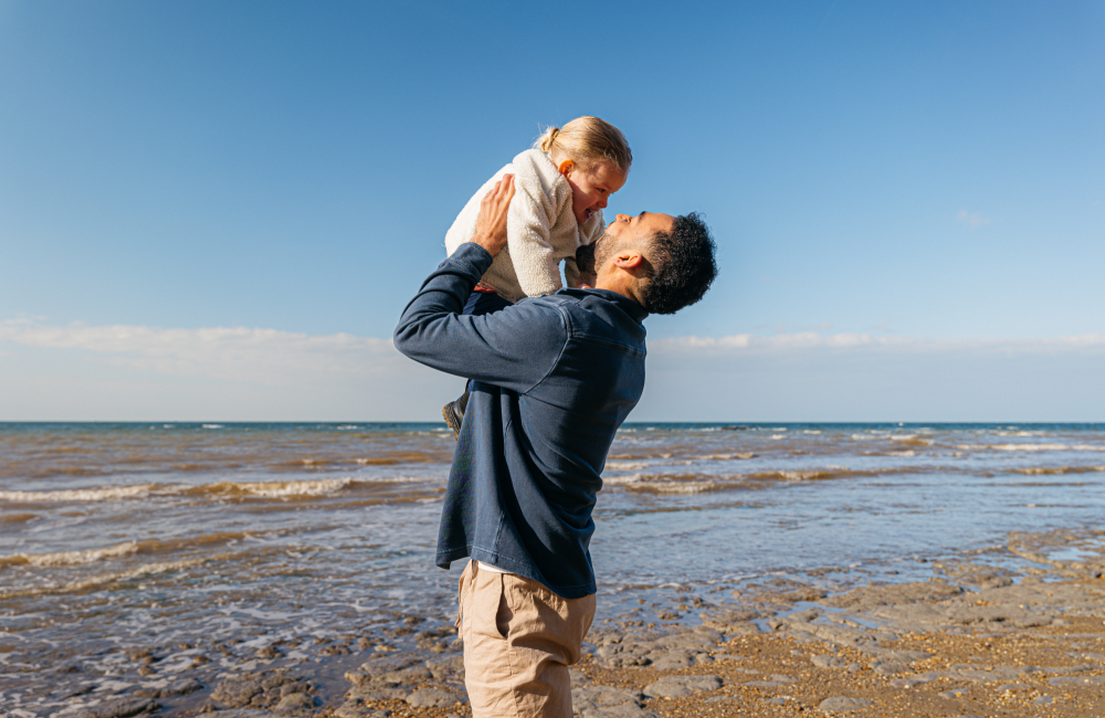 dad holds up young daughter on the beach